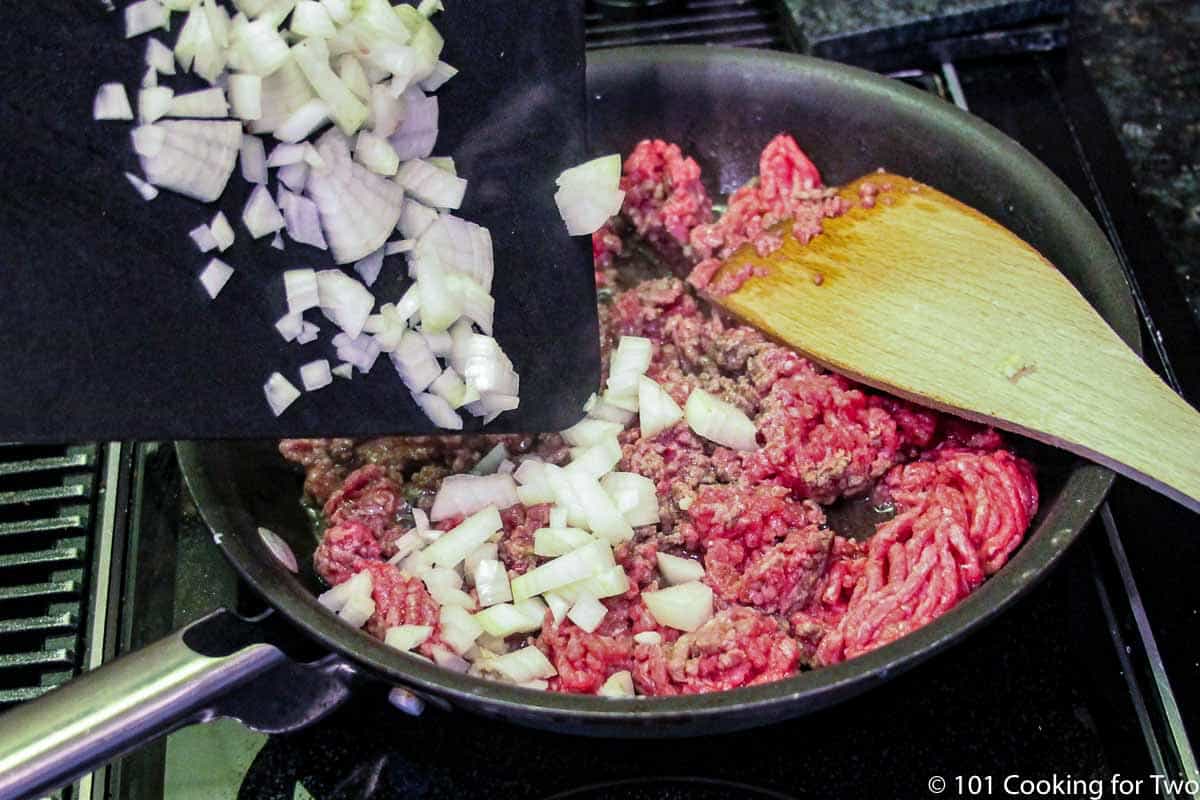 adding onion to burger in pan.