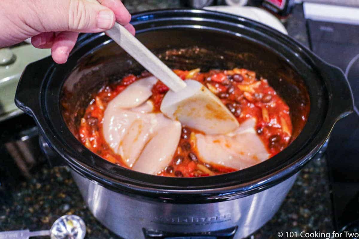 adding pieces of raw chicken to the cork pot with sauce and pasta