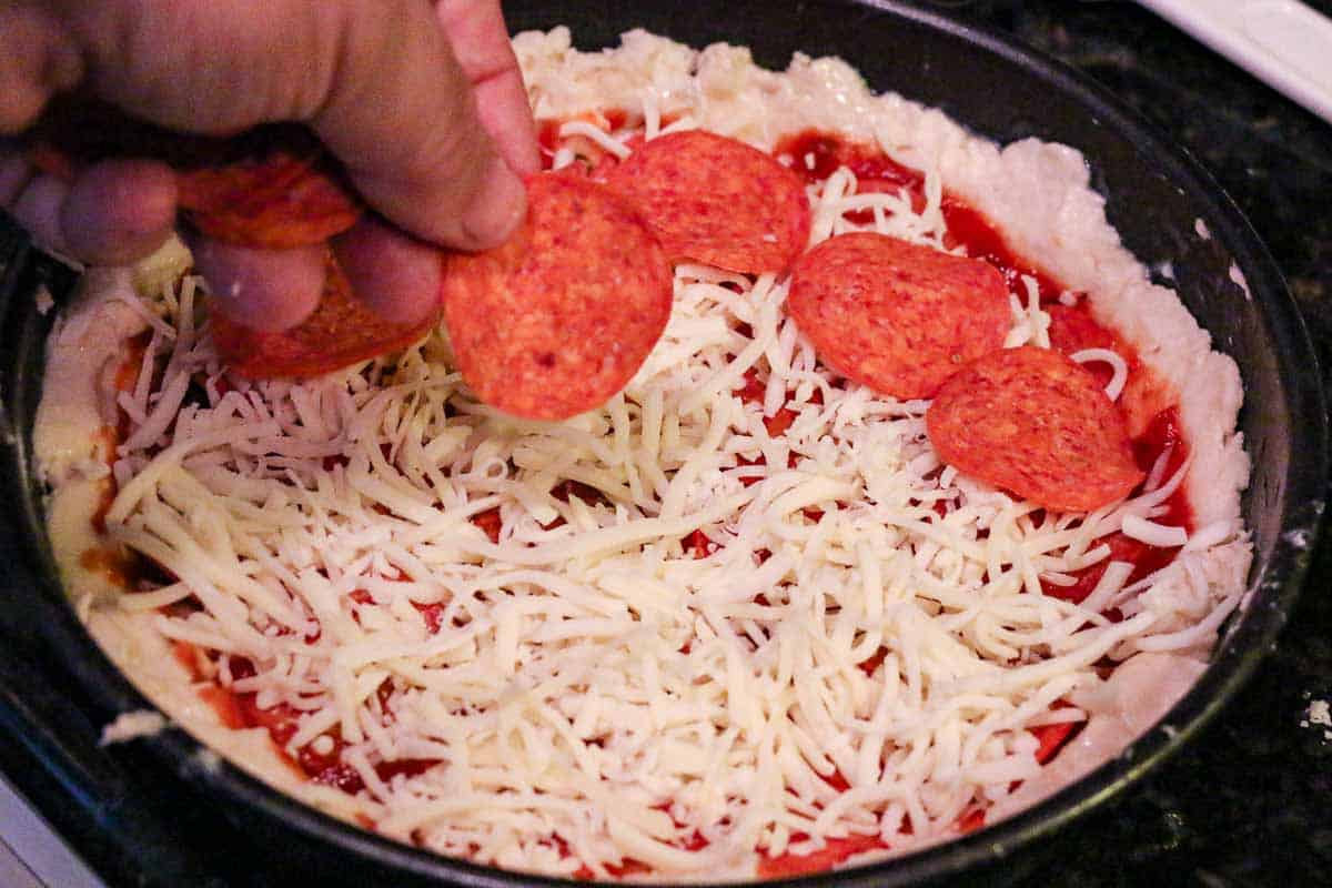 adding toppings on the pizza in a pan