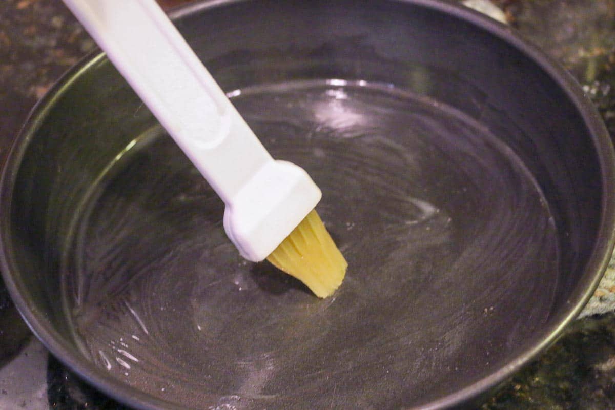 brushing a round black baking pan with butter