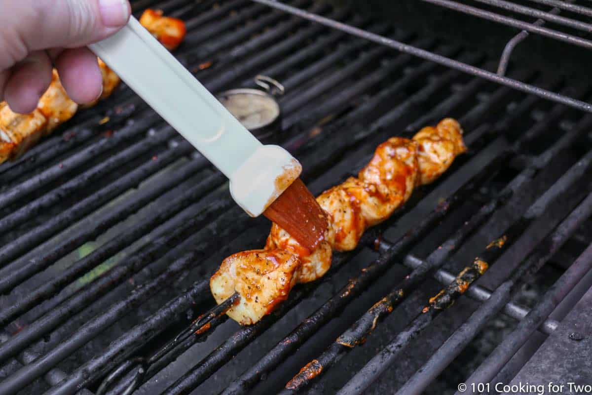 Brushing BBQ sauce on a cooking kabob on the grill grate.