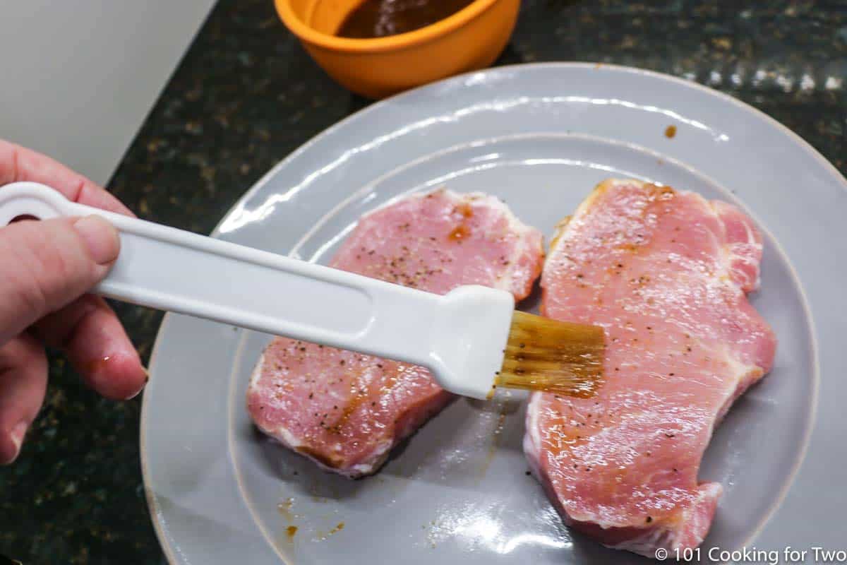 brusing glaze on raw pork chops on gray plate.