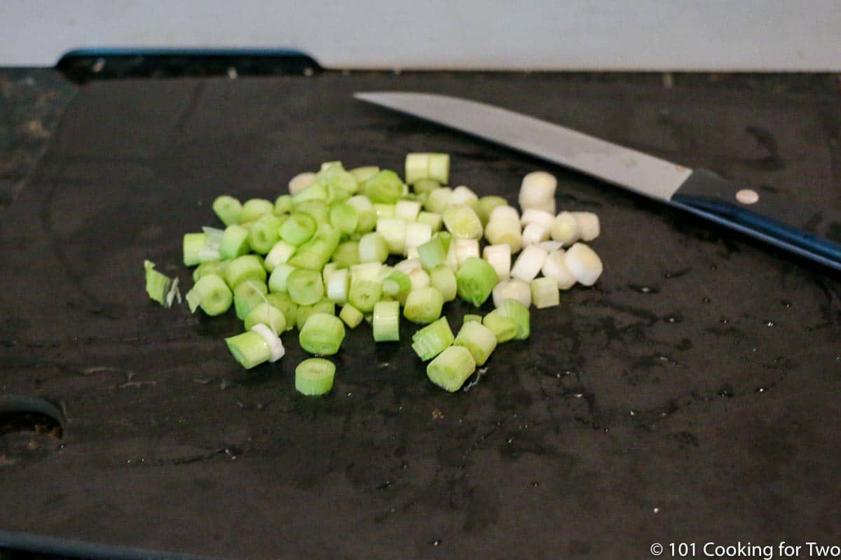 chopped green onion on black board.