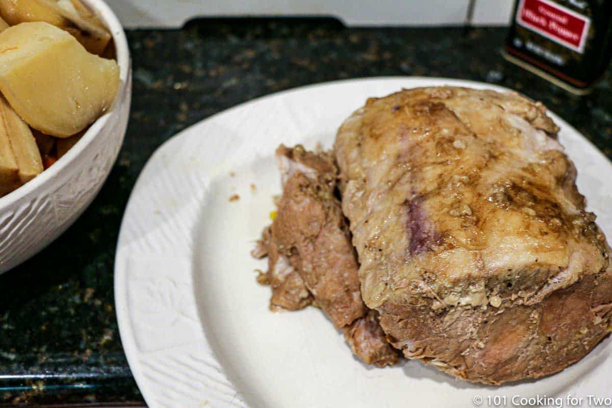 cooked pork roast on plate and bowl of veggies.