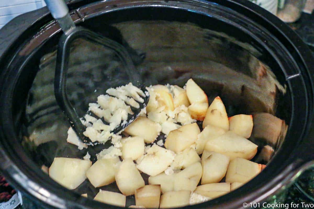 mashing e potatoes with a masher in the crock pot.