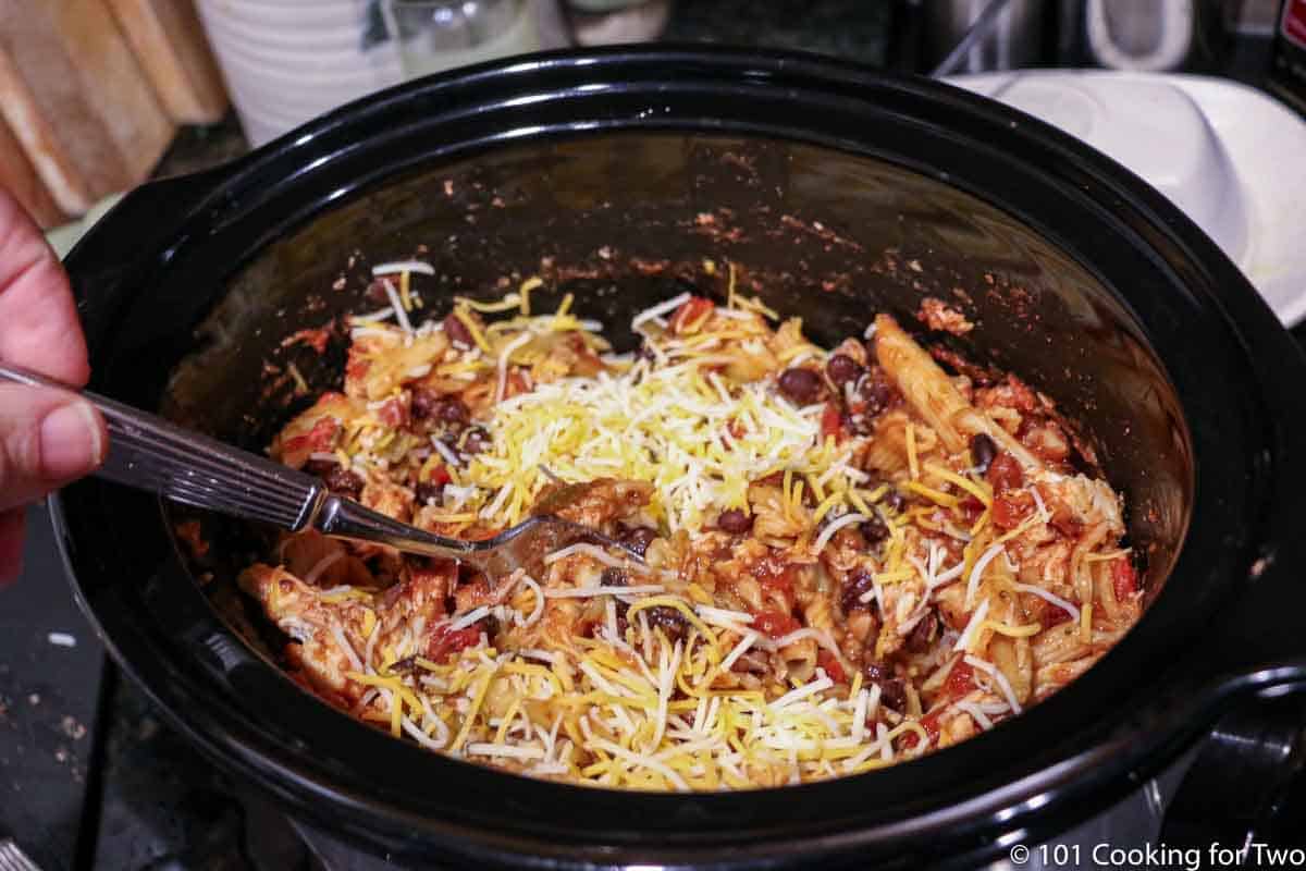 mixing shredded chicken and cheese into crock pot.