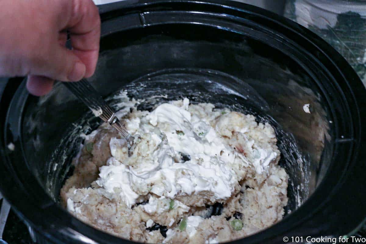 mixing sour cream into potatoes in crock pot.