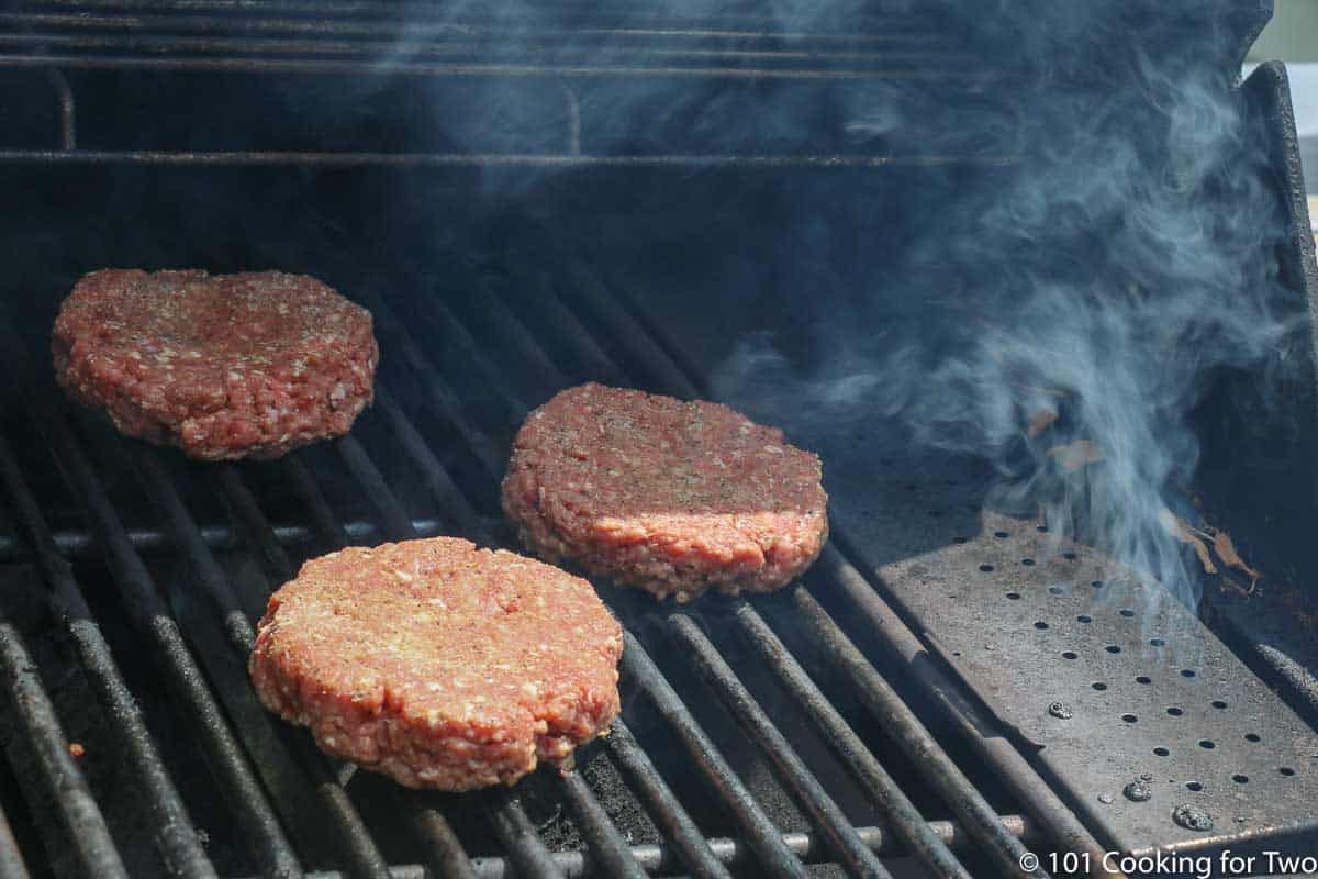 raw burgers on the grill with smoke starting