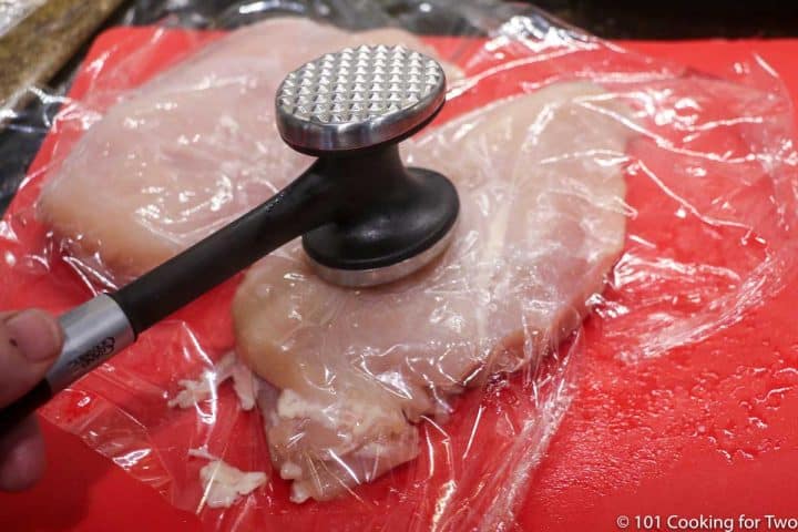 raw chicken on red board being hit with meat mallet