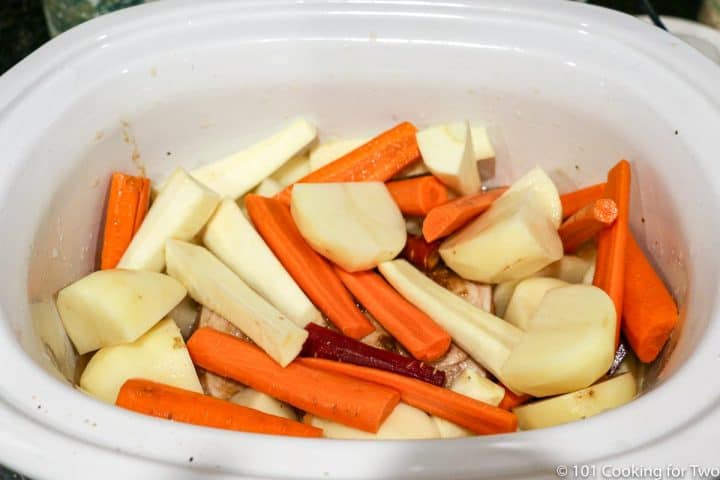 root vegetables piled on the pork loin in a crock pot