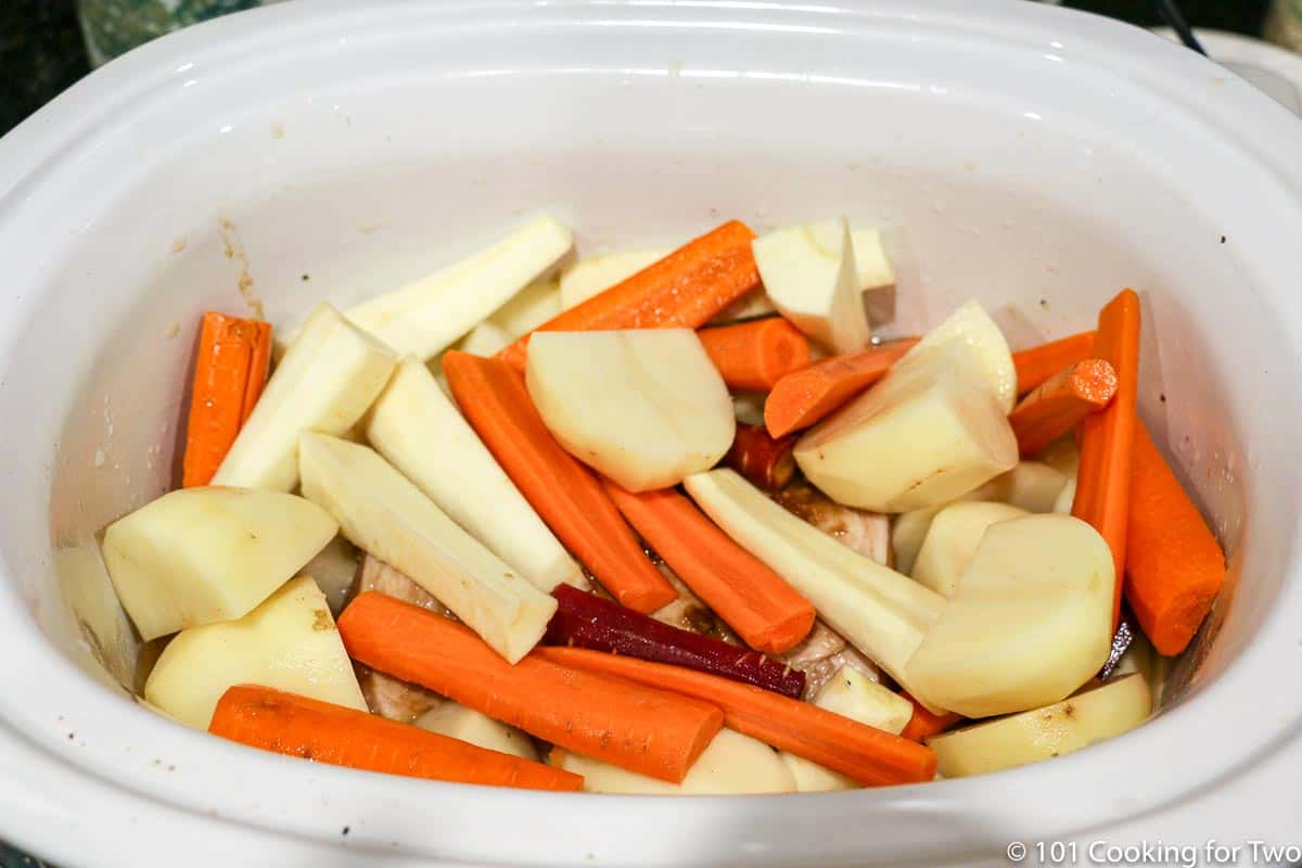 root vegetables piled on the pork loin in a crock pot.