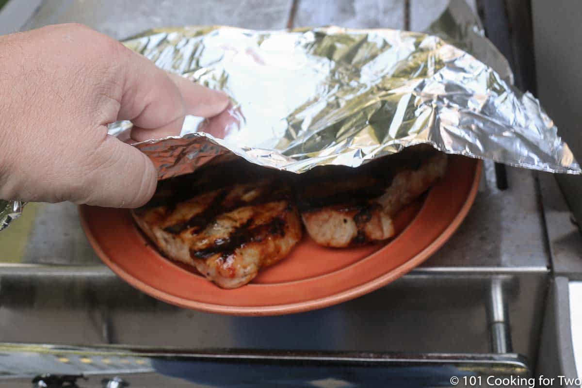 tenting pork chops on orange plate with foil
