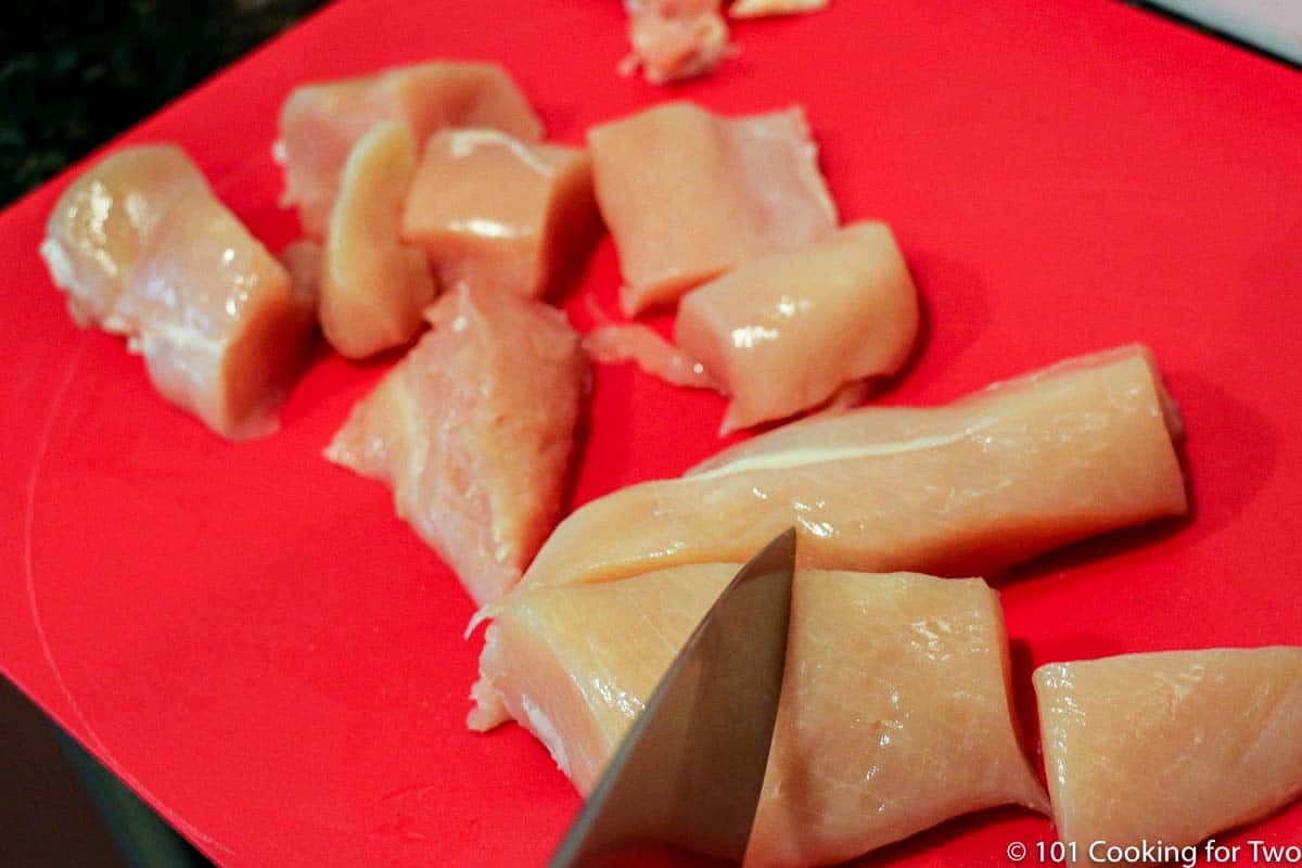 trimmed and cubed chicken on red board.