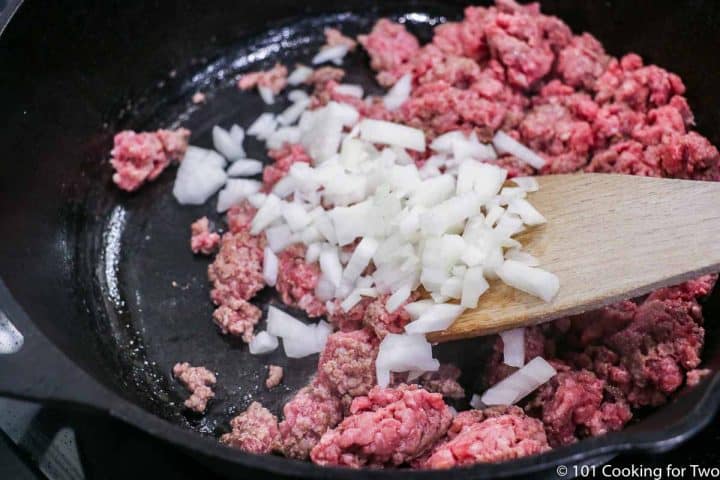 adding chopped onion to raw burger in a frying pan