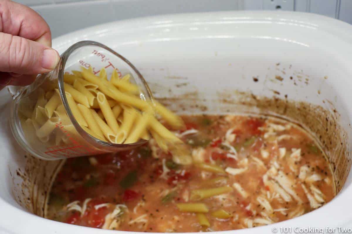 adding dry pasta to the crock pot with soup