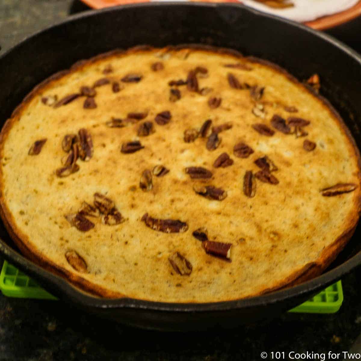 browned pancake in black pan with nuts on top