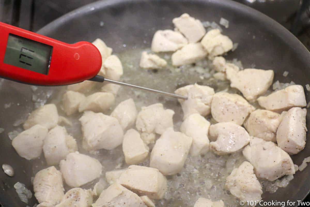 cooked chunks of chicken in pan with thermometer.