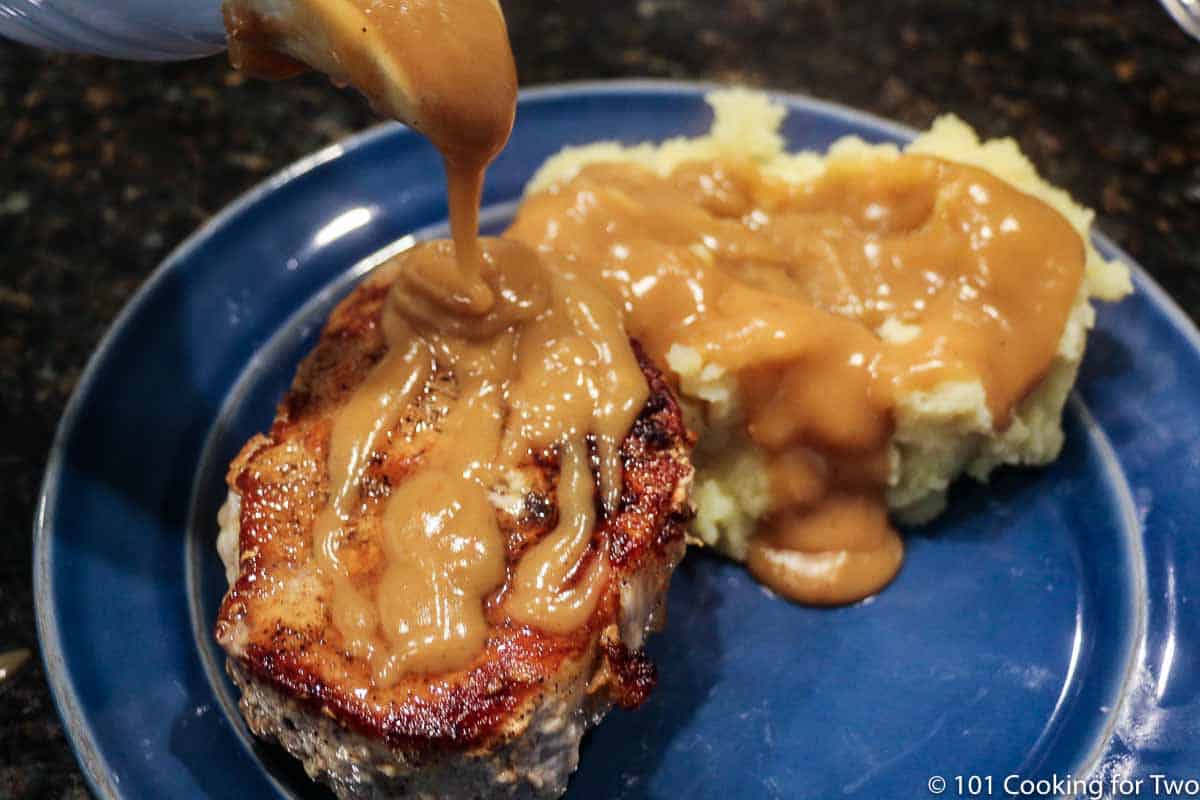 pouring gravy on pork chop and potatoes