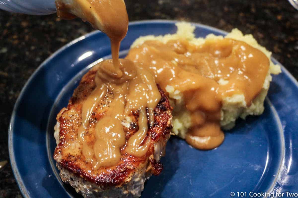 pouring gravy on pork chop and potatoes.
