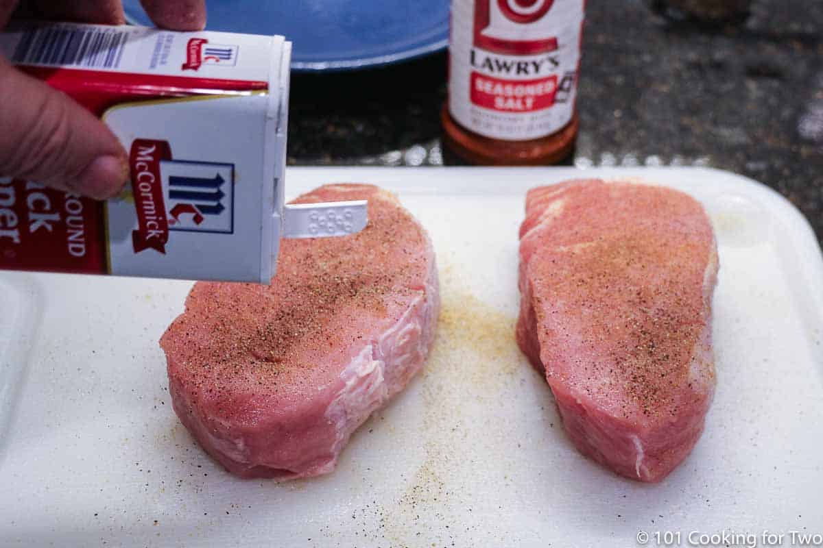 seasoning pork chops with pepper on white board