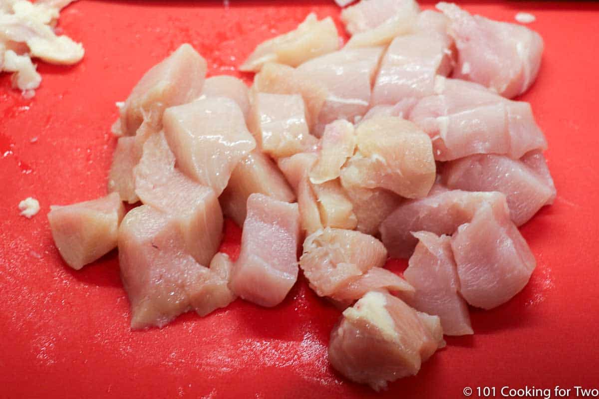 trimmed and chopped chicken on red board.