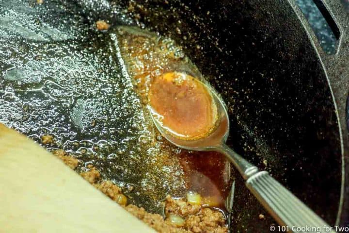 using a spoon to remove cooked fat from skillet