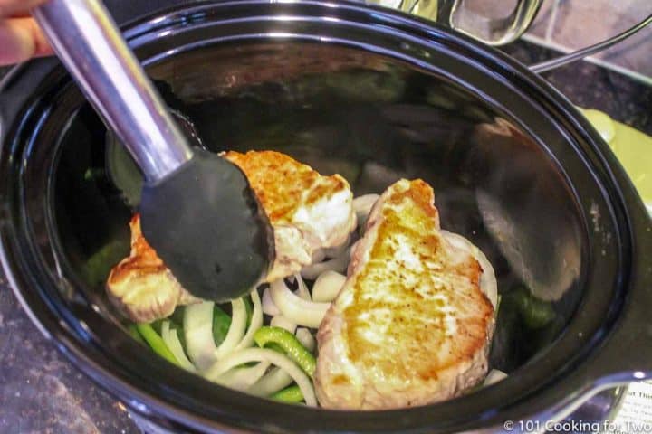 adding browned pork chops to crock pot with veggies