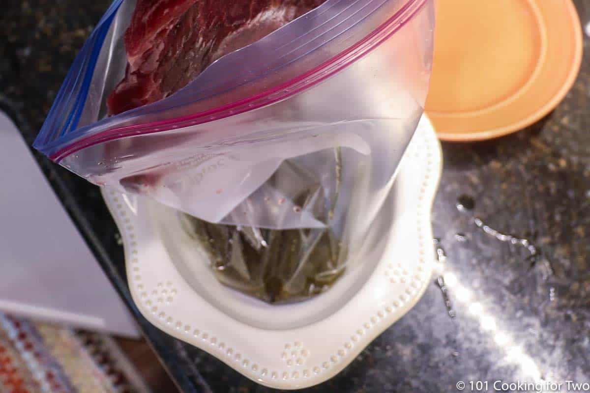 adding flank steak to bag with marinade.