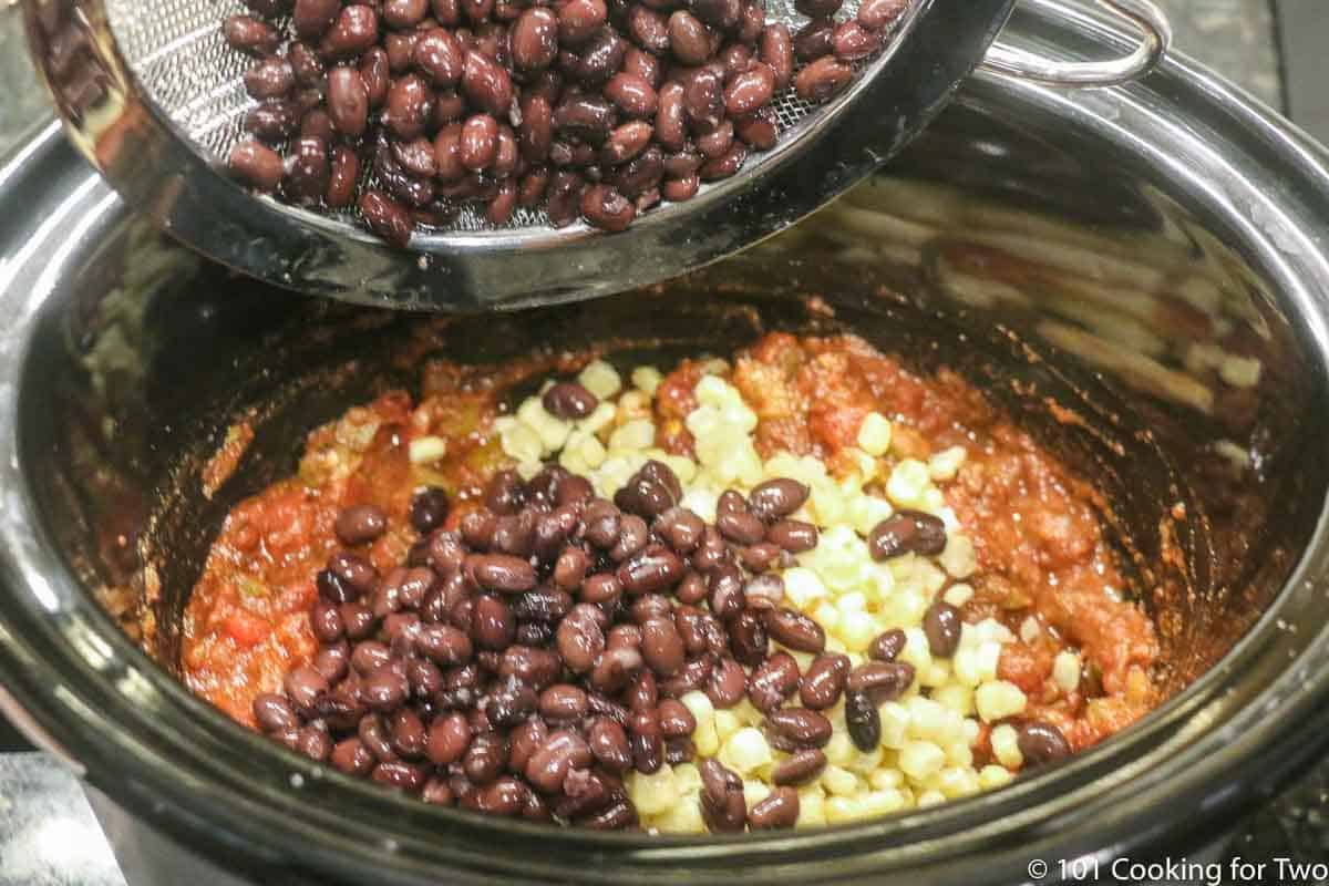 adding rinsed black beans to crock pot with corn and salsa
