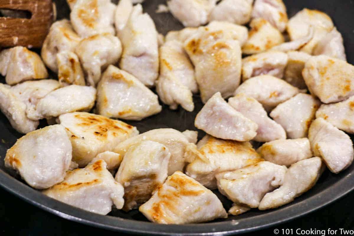 browning coated chicken in black pan.