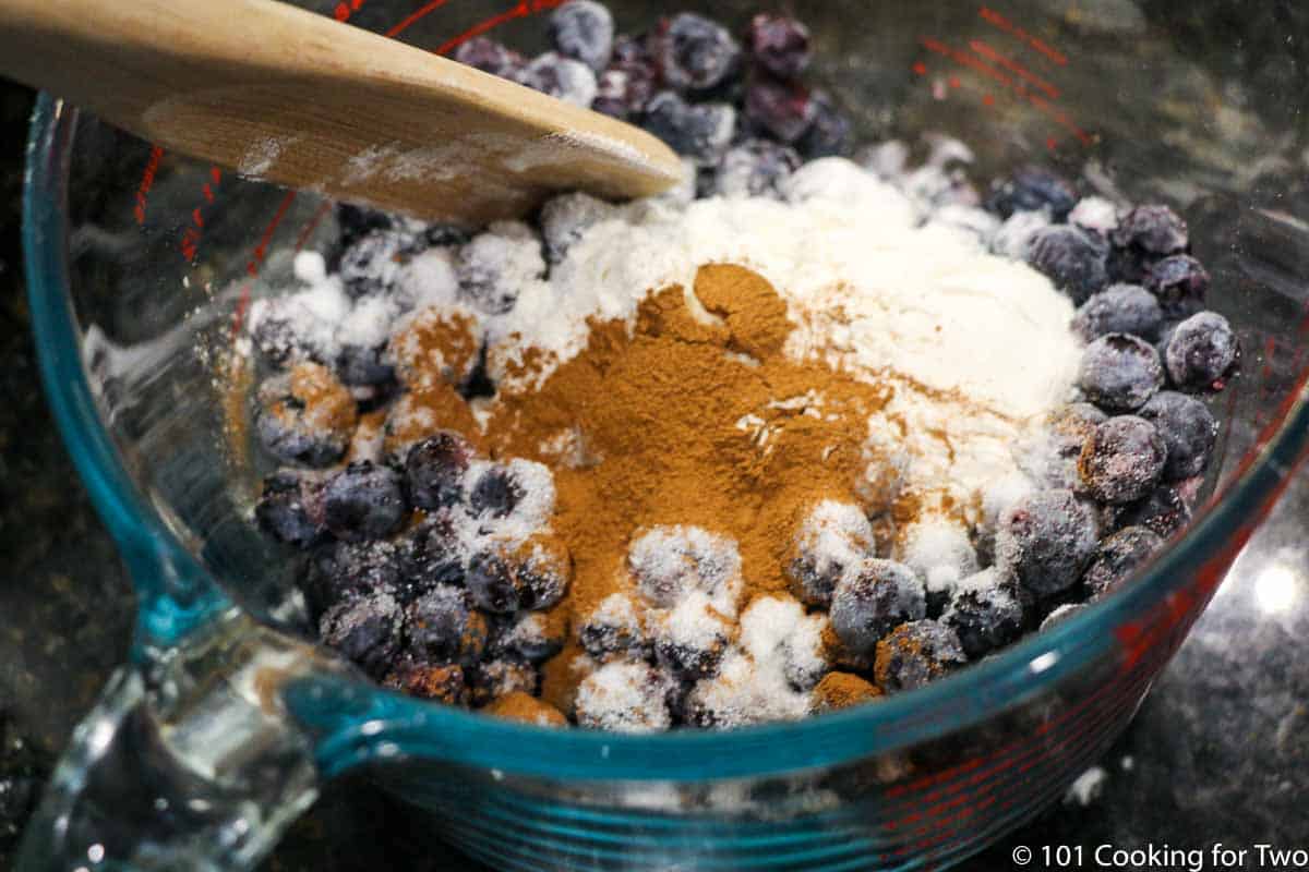 coating blueberries with sugar and cinnamon in bowl with wooden spoon.