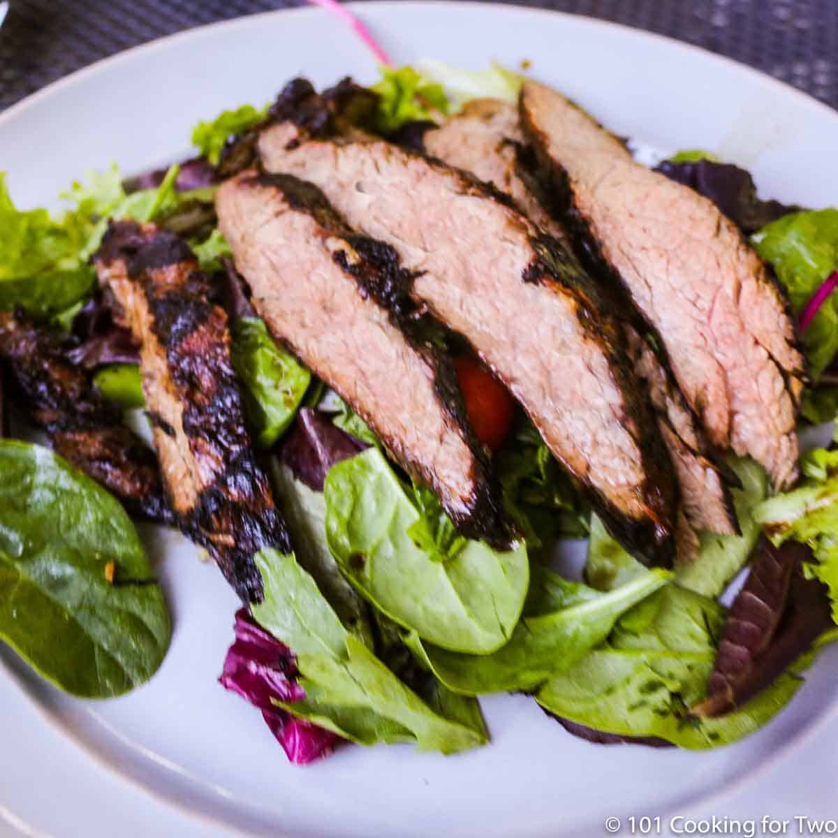 slices of grilled flank steak on salad