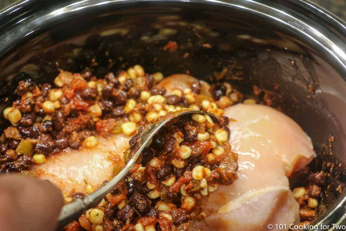 spooning corn and bean mixture over raw chicken in the crock pot