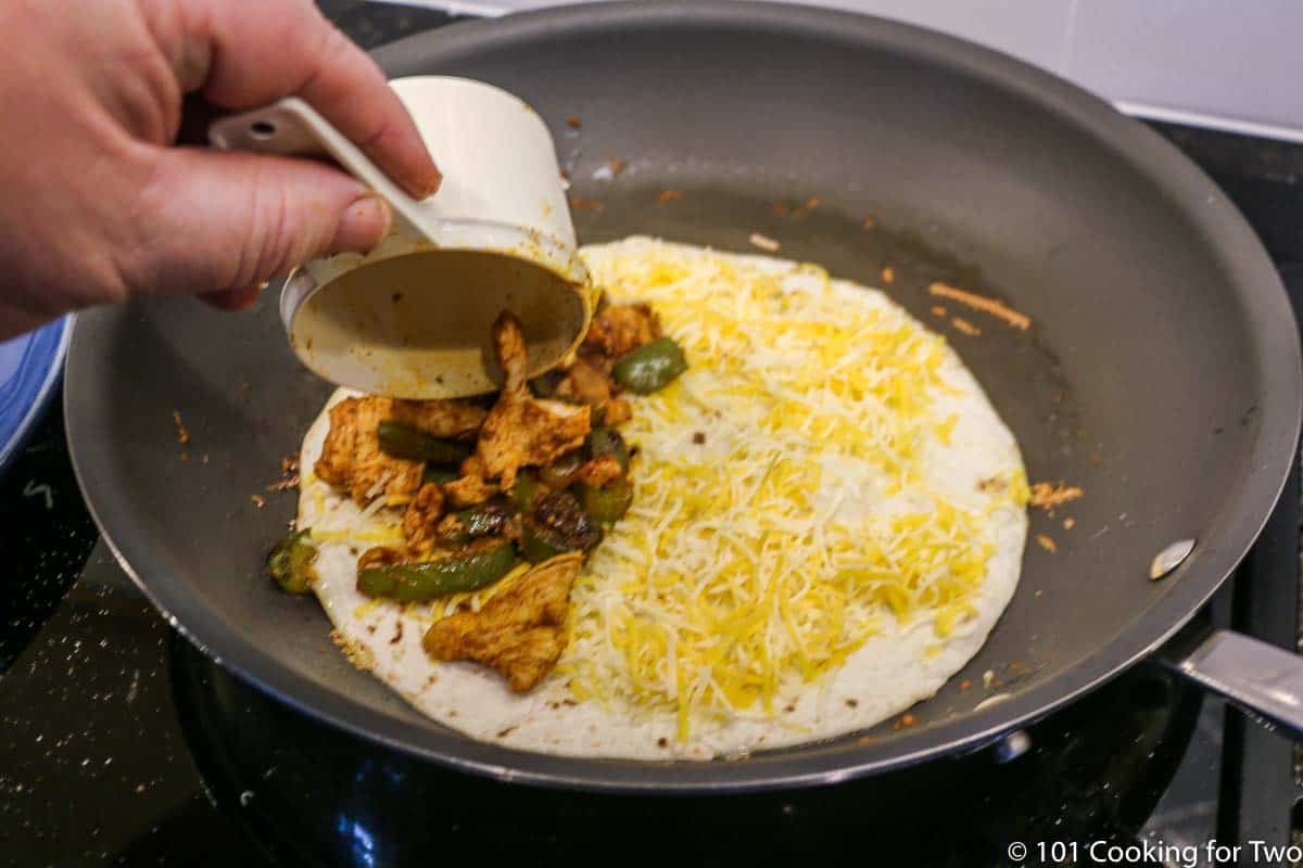 adding chicken mixture to totilla with cheese in skillet
