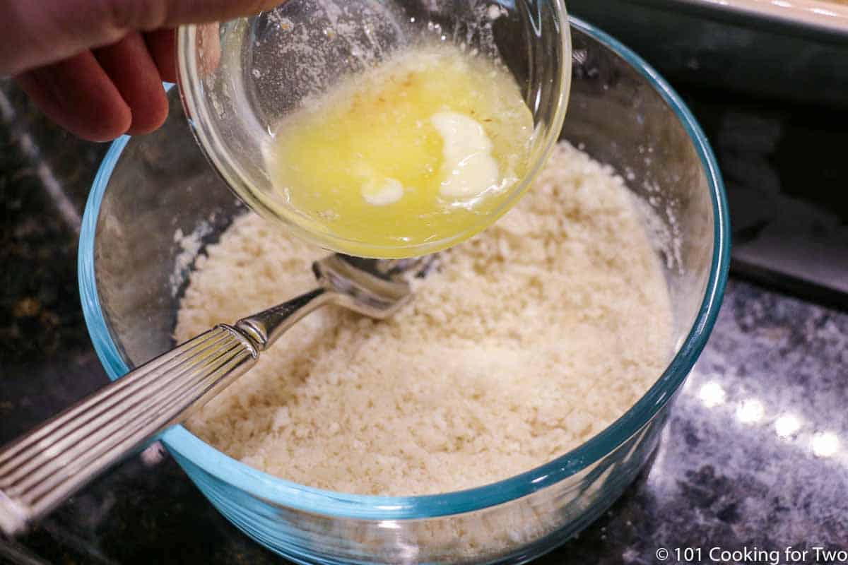 adding melted butter to bread crumbs in bowl.