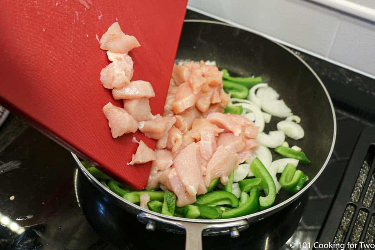 adding trimmed chicken to pan with pepper and onion.