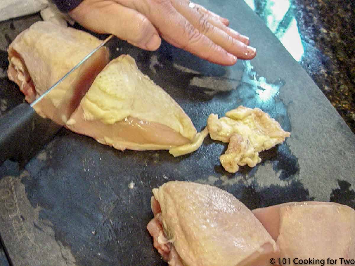 cutting a split chicken breast in half with knife.