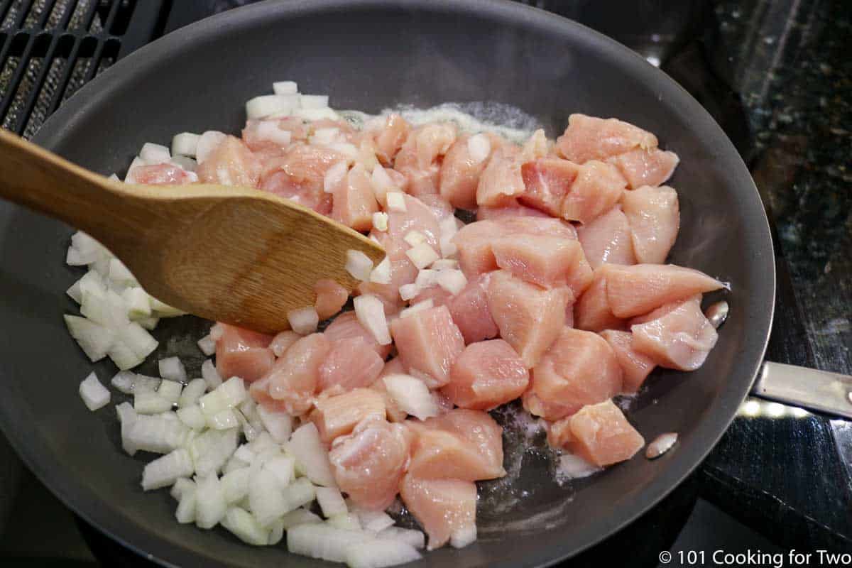 raw chicken and onion cooking in fry pan.