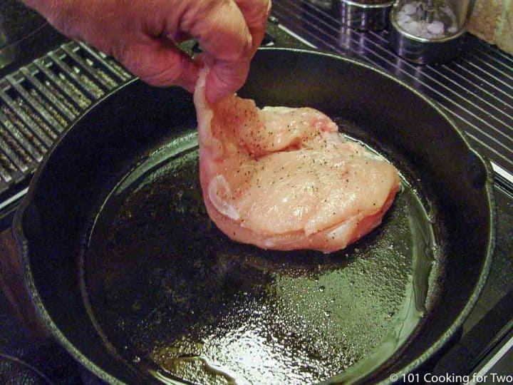 adding a seasoned chicken breast to a cast iron skillet with oil