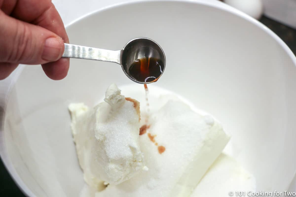 adding vanilla to bowl with sugar and cream cheese.