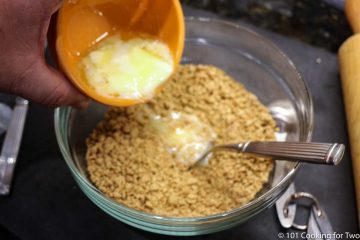 pouring melted butter into crushed crackers in glass bowl