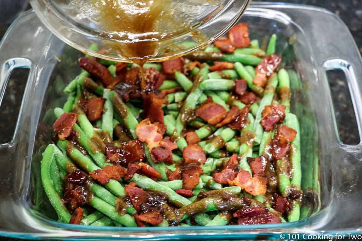 pouring topping over beans and bacon in baking dish.