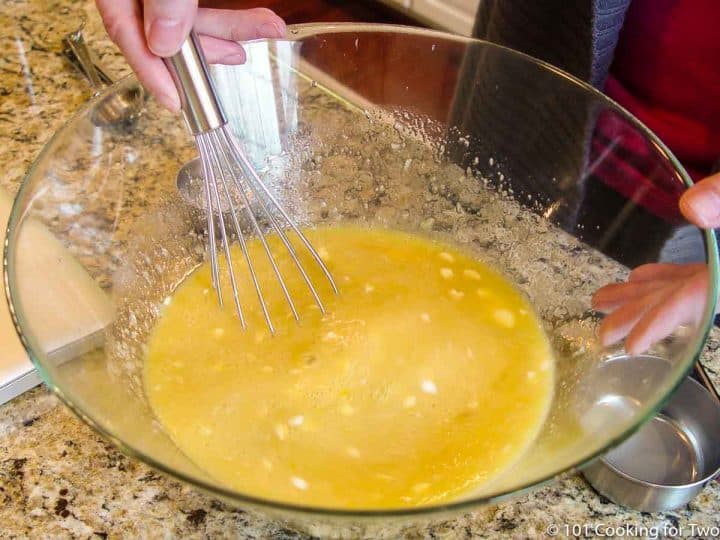 whisking eggs and other ingredients in white bowl