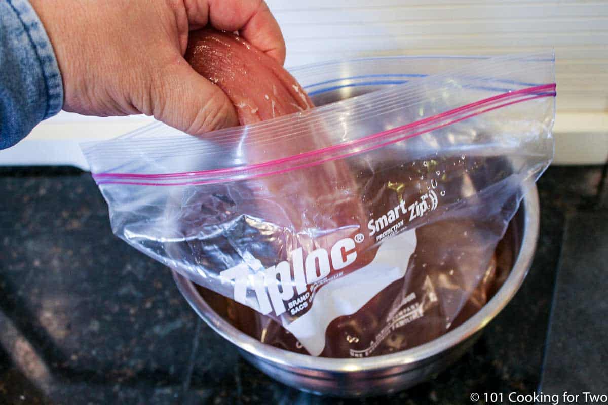 adding a pork tenderlion to a bag of brine in a metal bowl