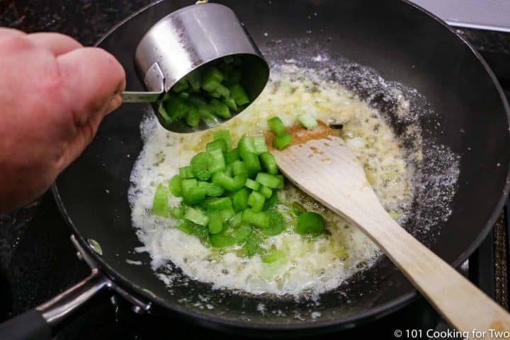 adding chopped celery to black pan making sauce