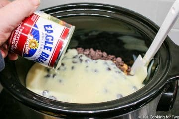 adding sweetened condensed milk to the crock pot with chocolate