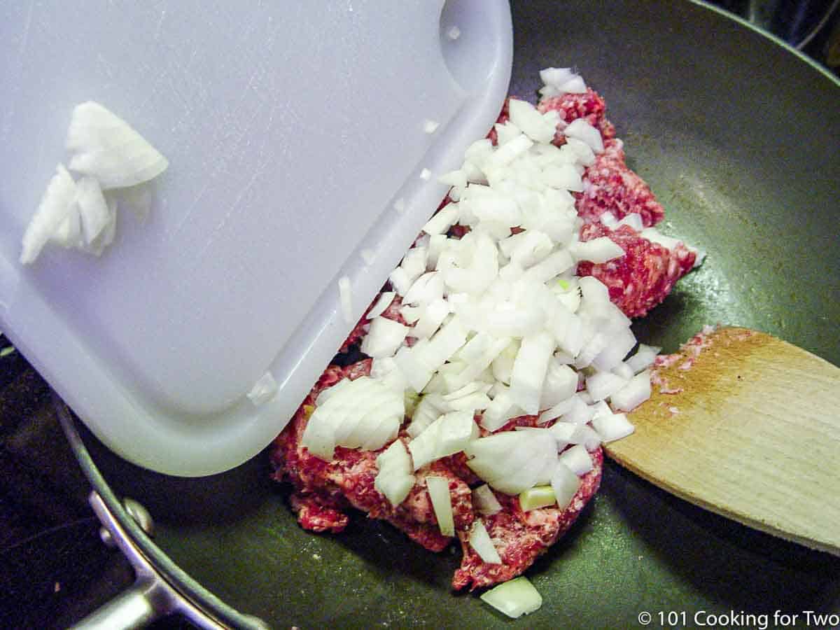 adding chopped onion to ground meat in pan.