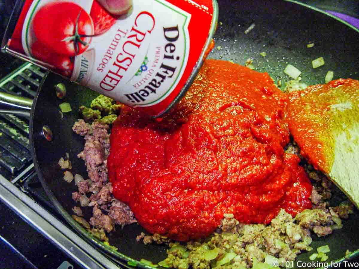 adding crushed tomatoes to cooked sausage in pan.