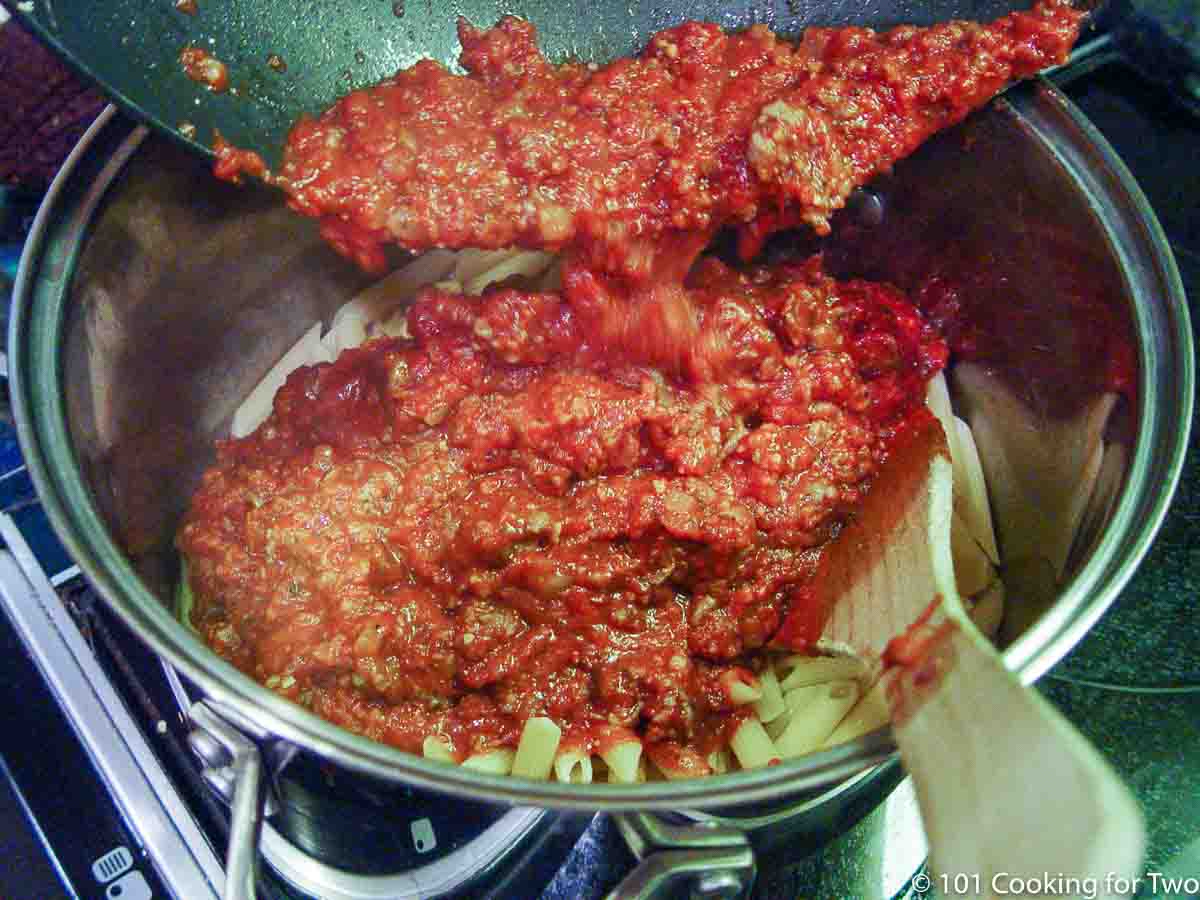 adding sause to cooked pasta in pan.