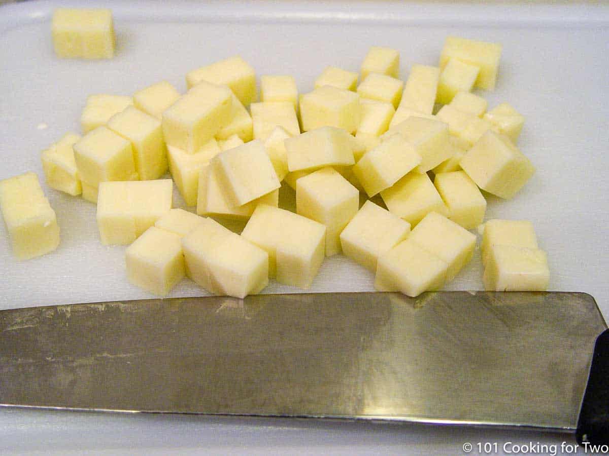 cheese chopped in cubes on white board.
